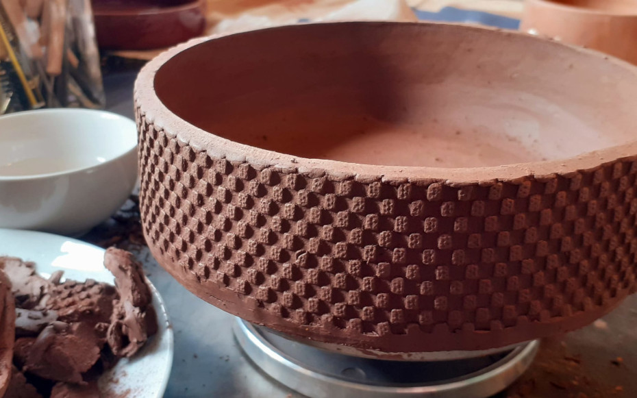 A clay pot with chequered pattern on a worktable.